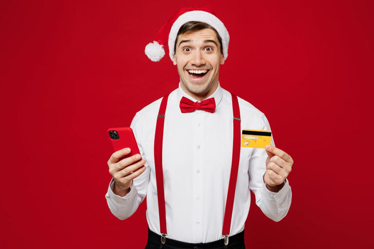 A cheerful man in a Santa hat holding a Christmas bonus announcement sign.